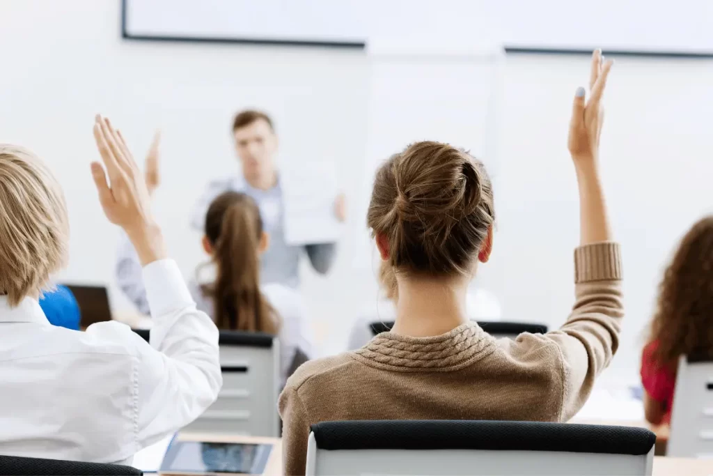 alunni alzano la mano mentre il docente fa domande