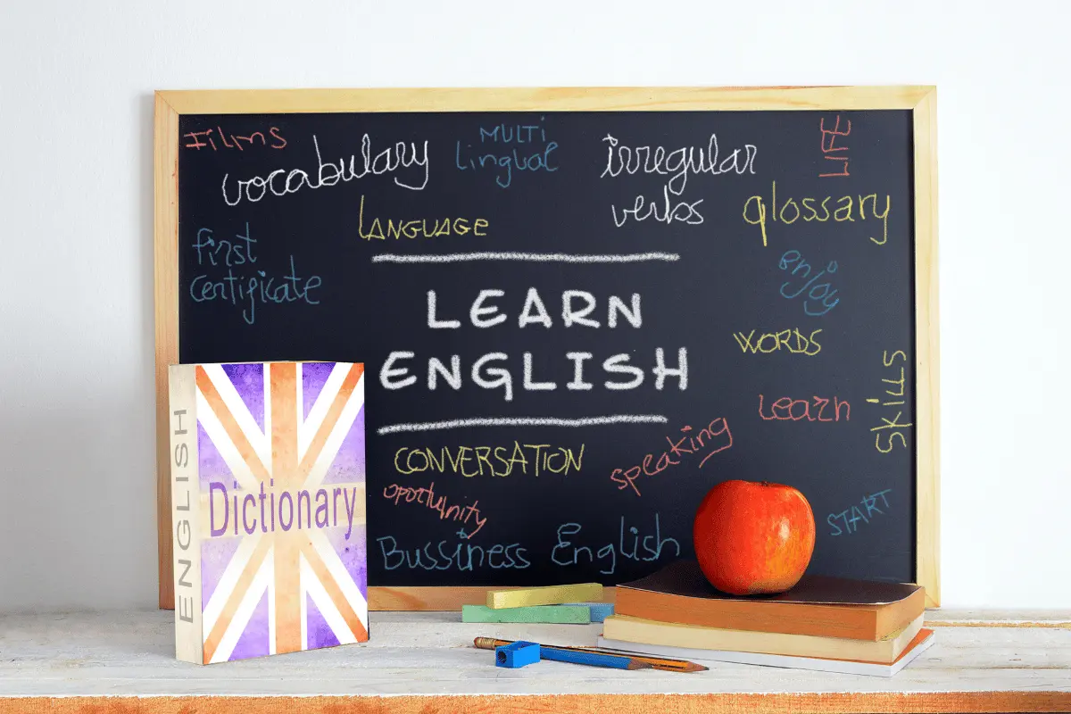 Vocabolario d'inglese davanti ad una lavagna con la scritta "Learn english"