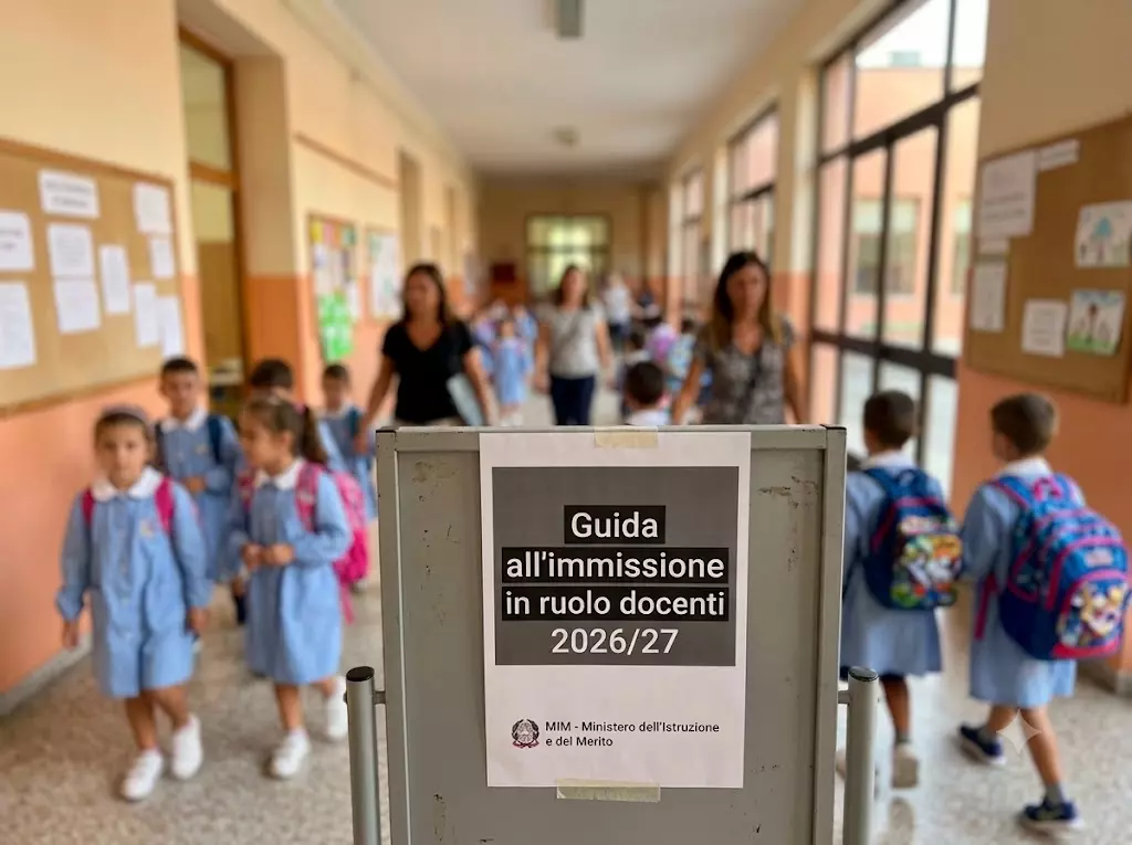Immissioni in ruolo docenti 2026/27: Docenti e alunni nel corridoio di una scuola. In primo piano la scritta: "Guida all'immissione in ruolo docenti 2026/27"
